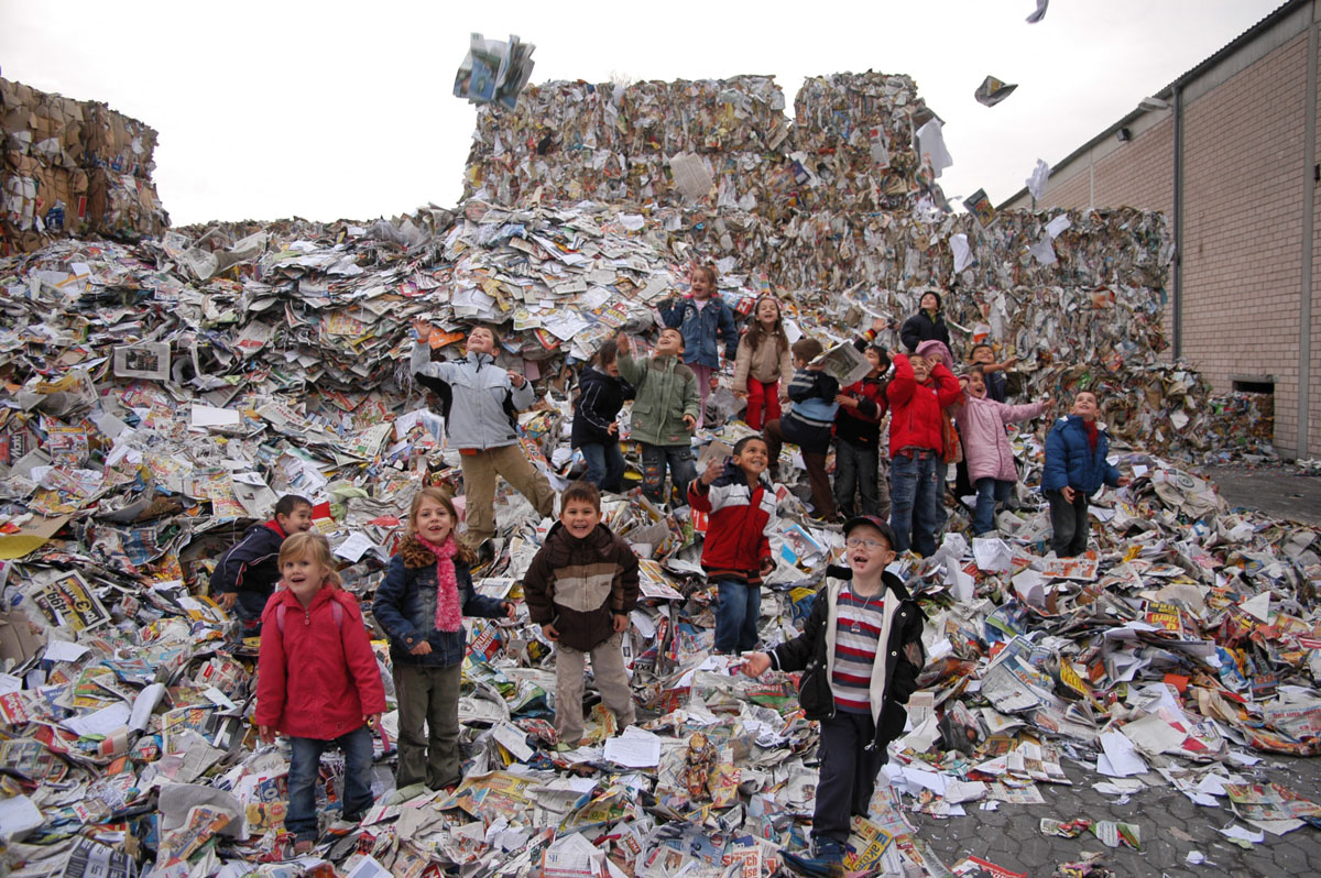 Papierrecycling hautnah: Schulkinder auf einem Papierberg inmitten von Papierballen