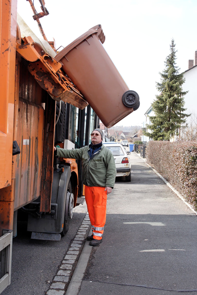 Modernes Einzelgänger-Müllfahrzeug: Müllwerker leert braune Biotonne mit der Seitenladertechnik