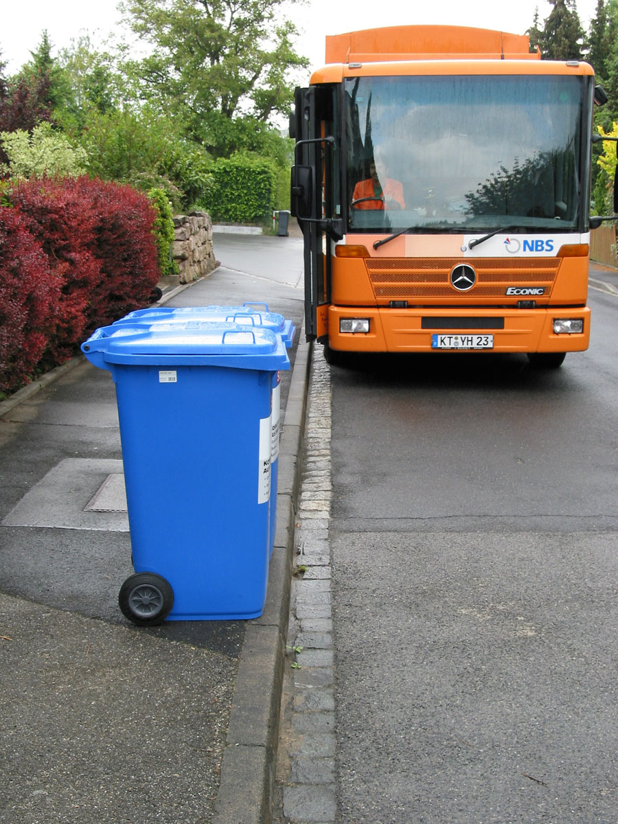 Abfuhr Papiertonne mit orangem Seitenlader-Müllfahrzeug: Blaue Papiertonnen (MGB 240 Liter), Straßenrand, Gehsteig