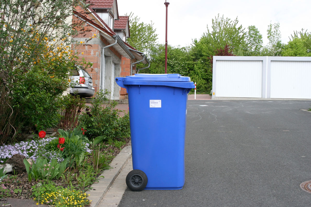 Blaue Papiertonne (MGB 240 Liter) wartet am Straßenrand auf die Müllabfuhr
