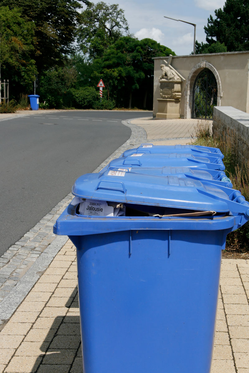 Blaue Papierabfallbehälter MGB 240 Liter stehen am Gehsteig (Fußweg) zur Abfuhr bereit: Leerung, Straße, Papiertonne leicht überfüllt