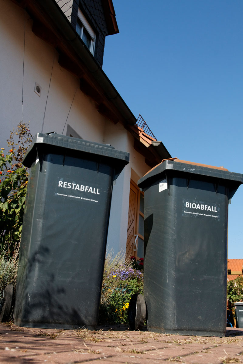 Mülltonnen am Haus auf dem Grundstück: Restabfalltonne und Biotonne mit grauem Rumpf (Korpus)