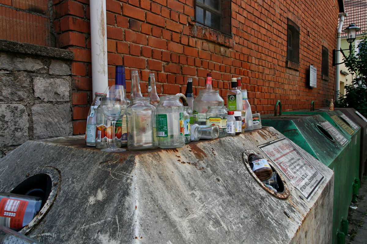 Uneinsichtige Zeitgenossen stellen Konservengläser, Flaschen, Trinkgläser auf einem überfüllten Glascontainer ab