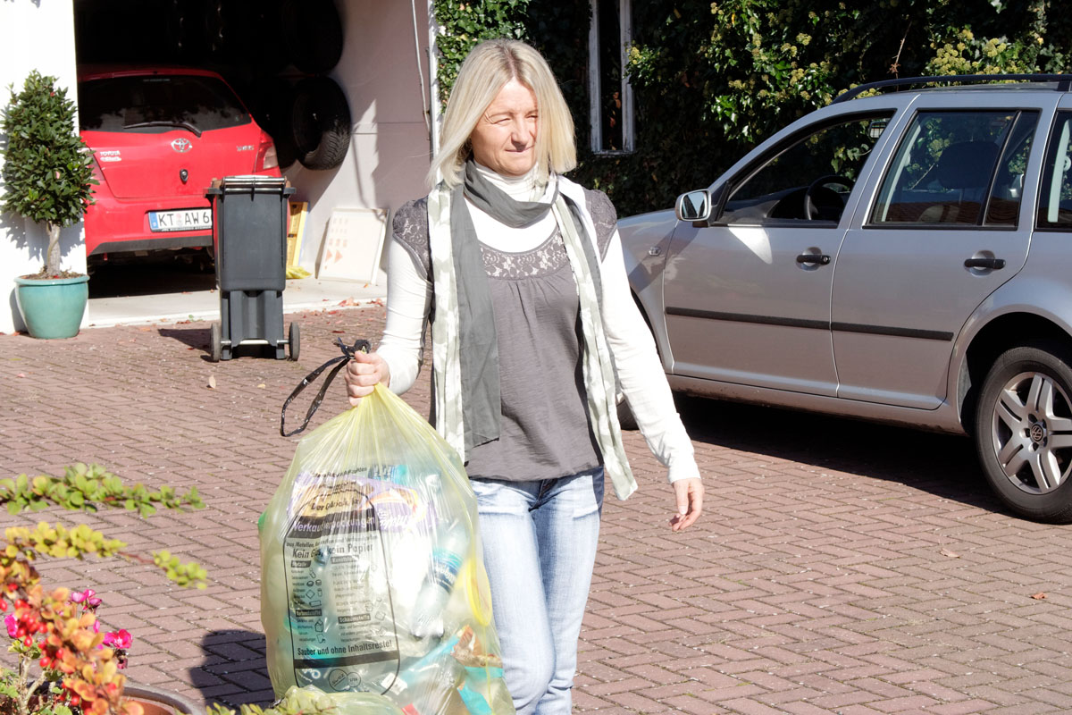 Bald kommt die Müllabfuhr: Frau trägt Gelben Sack an den Straßenrand