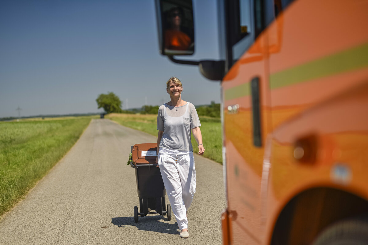 Biotonne, oranges Müllfahrzeug, Frau, Bereitstellung zur Müllabfuhr, Mülllaster, Müllauto