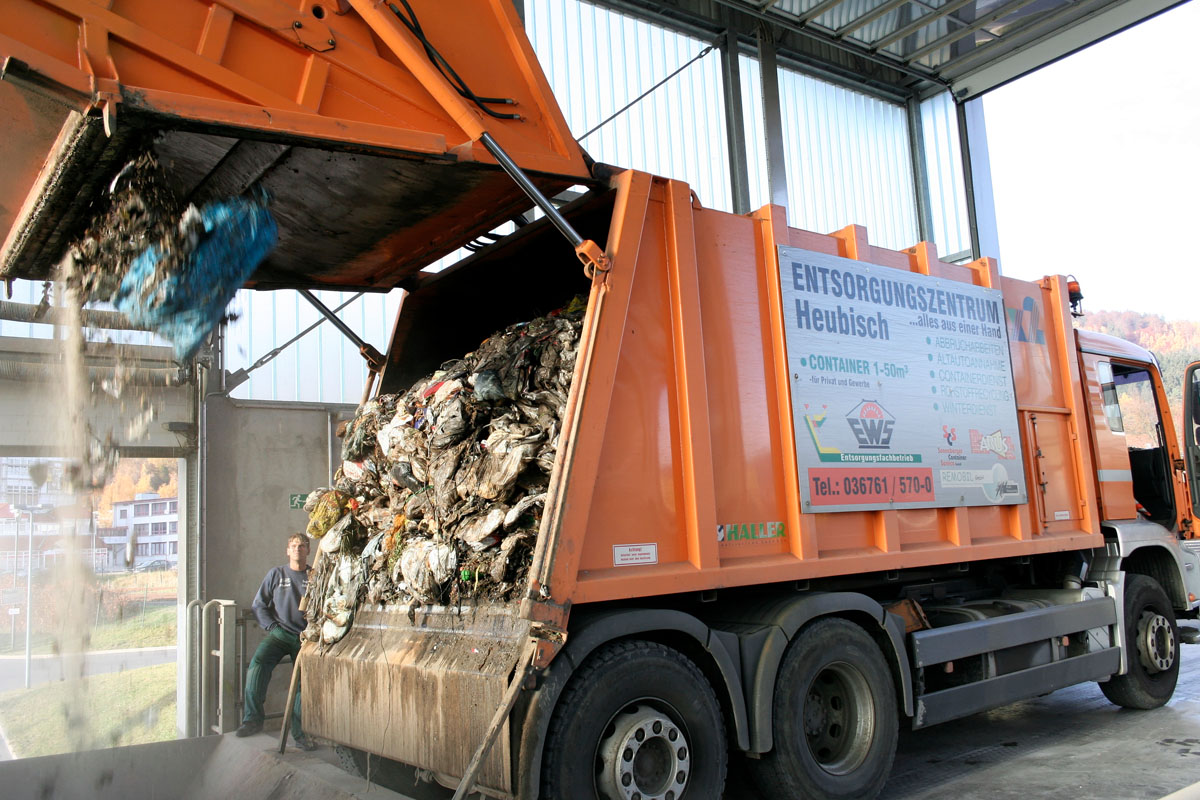 Abkippen, Abladen, Entladen in der Müllumladestation: Oranges Hecklader-Müllfahrzeug entleert Restmüll in einer Halle