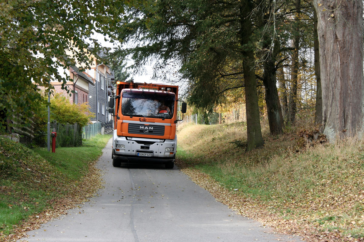 Die Müllabfuhr kommt: Oranges Müllfahrzeug vom Typ Hecklader im Thüringer Wald
