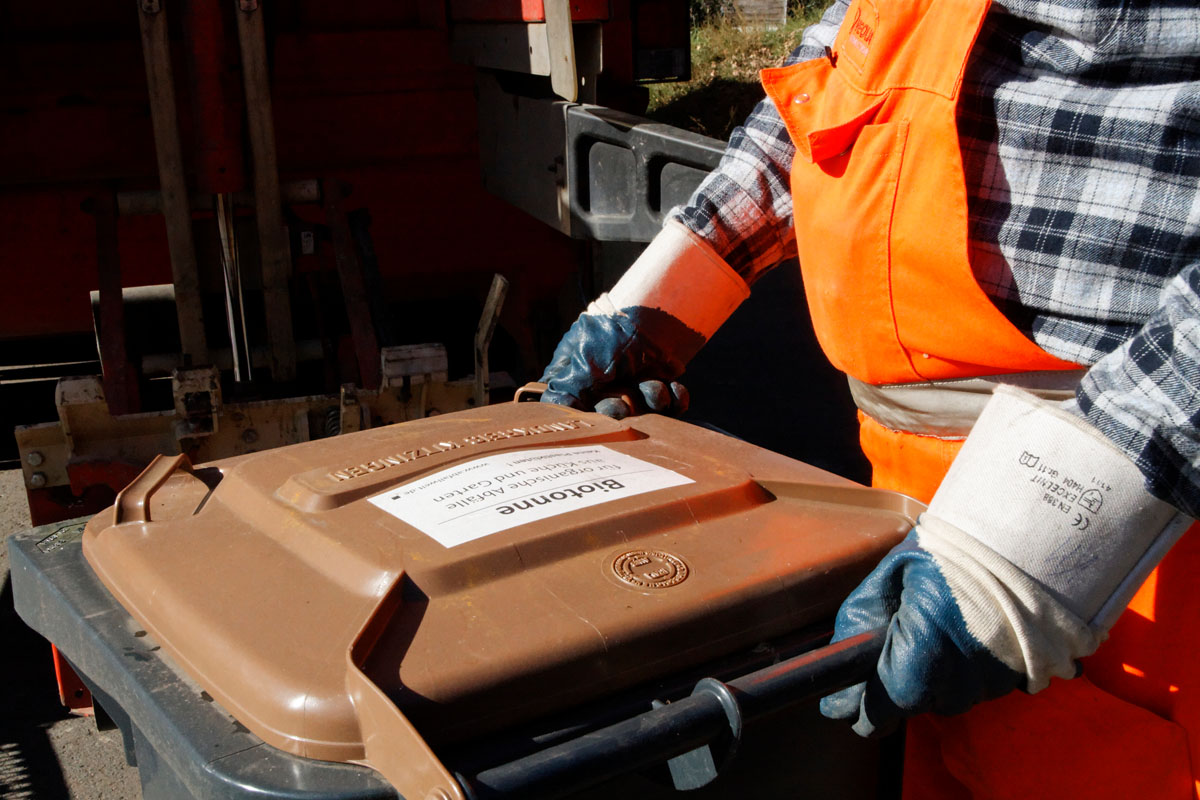 Müllmann in Orange schiebt Biotonne zur Schüttung des Müllfahrzeugs