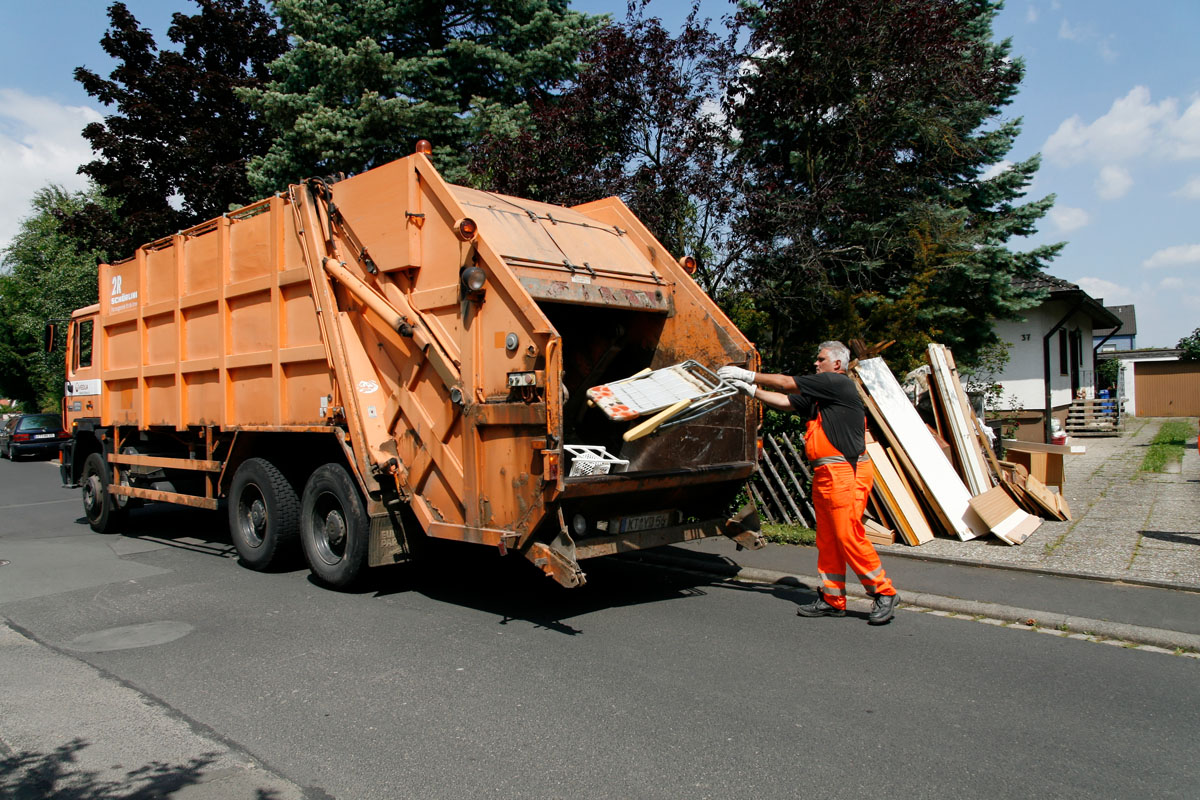 Sperrmüllabfuhr: Müllwerker in oranger Arbeitskleidung lädt Gartenstuhl in das Hecklader-Müllfahrzeug