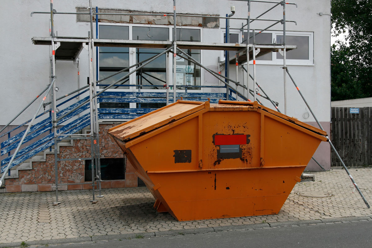 Container für Bauschutt: Orange Deckelmulde, Gerüst, Hausfassade, Gehsteig, Renovierung