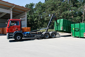 Große Mülltransportcontainer: Container-LKW lädt Abrollbehälter/Gleitabsetzbehälter (GAB) an einem Wertstoffzentrum auf