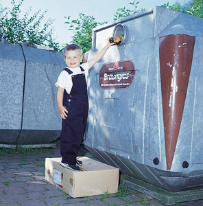 Wertstofftrennung am Containerstandort: Junge wirft Flasche in einen Braunglascontainer