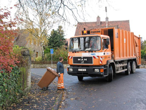 Biomüllabfuhr: Müllwerker bringt eine braune Biotonne zum Müllfahrzeug