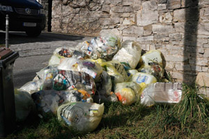 Gelbe Säcke warten auf ihre Abholung: Steinmauer, Ortschaft, Grasstreifen, Grünfläche