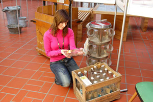 Abfallvermeidung in alter Zeit: Junges Mädchen betrachtet Mehrweg-Glasflaschen in einem Holzkasten