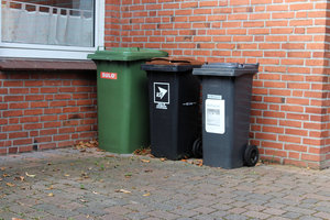 Mülltonnen an einer Hauswand: Restabfalltonne 120 Liter MGB, Biotonne 120 Liter MGB, grüne Papiertonne 240 Liter MGB, Backsteinhaus