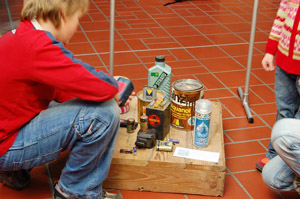 Kinder betrachten Problemmüll-Exponate der Abfallausstellung: Batterien, Farbdosen, Öldose, Spraydose