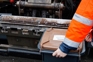Müllabfuhr: Müllwerker hängt Biotonne in die Schüttung eines Hecklader-Müllfahrzeugs ein