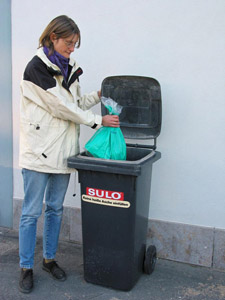 Frau wirft Mülltüte in eine graue Restmülltonne