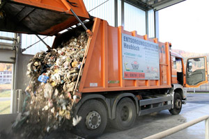 Oranges Hecklader-Müllfahrzeug entlädt den Müll in einer Umladestation: Ausladen, Müllschacht, offenes Heckteil