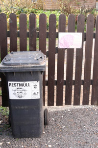 Graue Restabfalltonne (MGB 120 Liter) mit Hinweisaufkleber «Restmüll» vor einem Gartentor