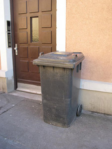 Ich muss draußen bleiben: Graue Restmülltonne neben einer Haustür in der Stadt