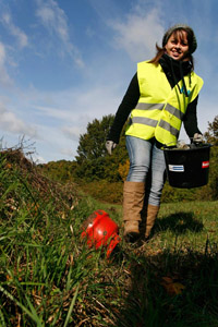 Flurreinigungsaktion: Mädchen, Eimer, gelbe Warnweste, Handschuhe,Topf, Landschaft, Sammelaktion, illegaler Müll, wilder Müll, junge Frau