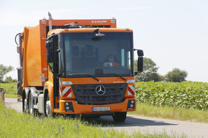 Modernes oranges Müllfahrzeug, Mülllaster, Frontansicht, asphaltierter Feldweg, Natur